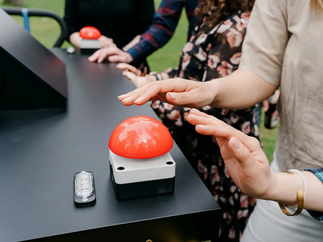 Hände schweben über dem roten Buzzer der Quizstation