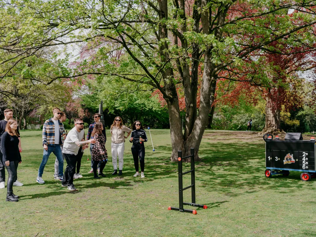 Eine Gruppe spielt Leitergolf auf einer Wiese, daneben steht der Battle-Wagen